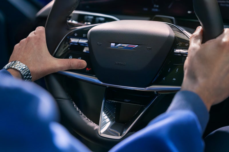 Close-up of a Man About to Press the V-Button on the 2026 OPTIQ-V Steering Wheel | Bridgeton Cadillac in Bridgeton NJ